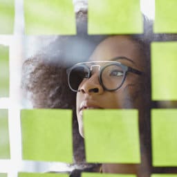 Portrait of a business woman with an afro behind sticky notes in bright glass office